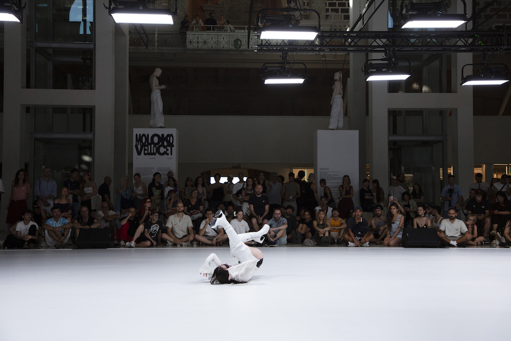 una performer vestida de blanco realiza una voltereta