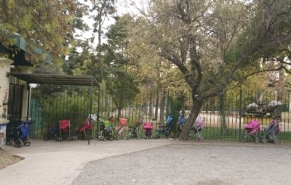 motherhood and artistic practice - Row of parked strollers beside a fence.